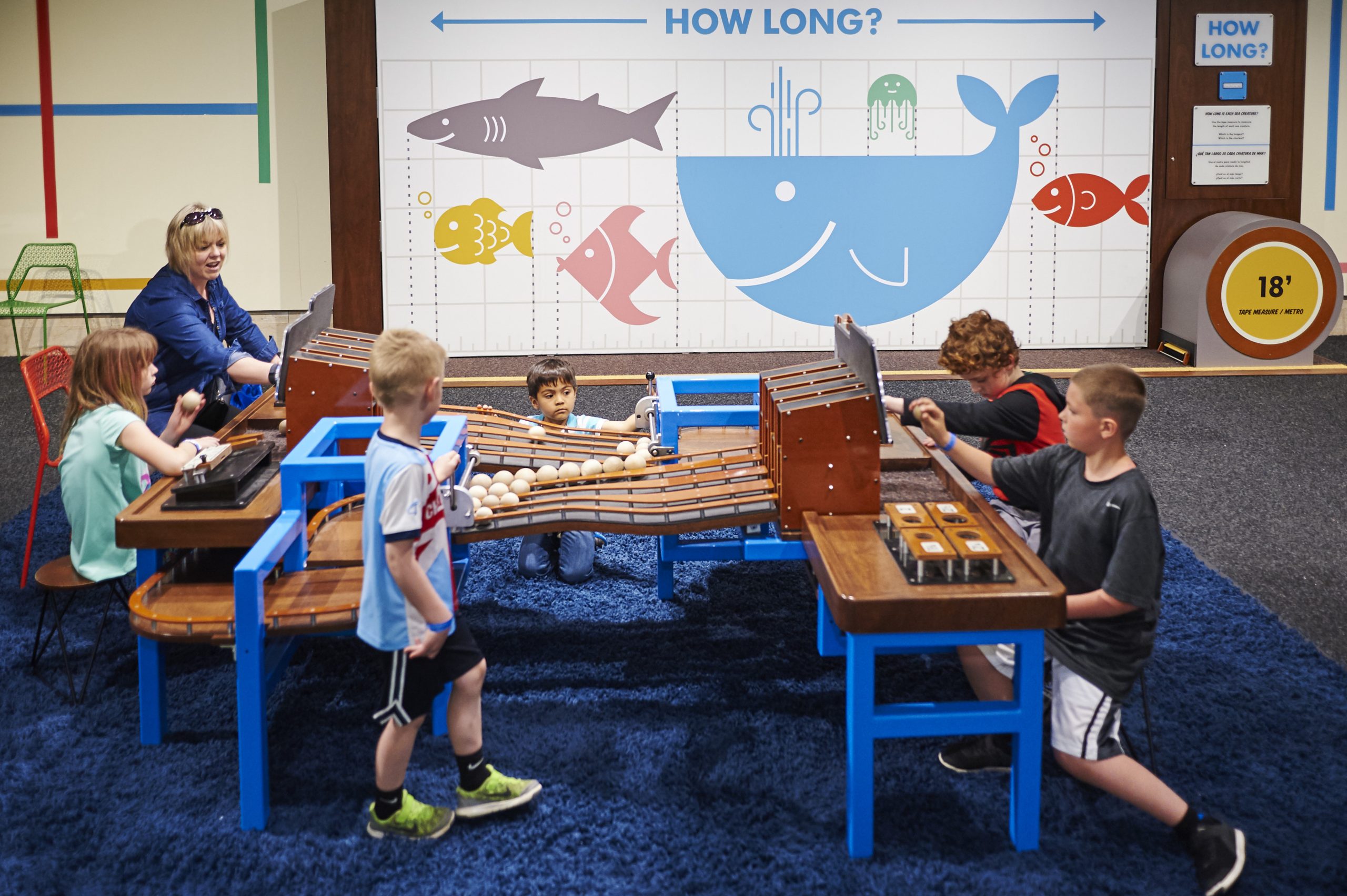 Family sitting down at tables testing, experimenting, measuring in front of a large whale mural.