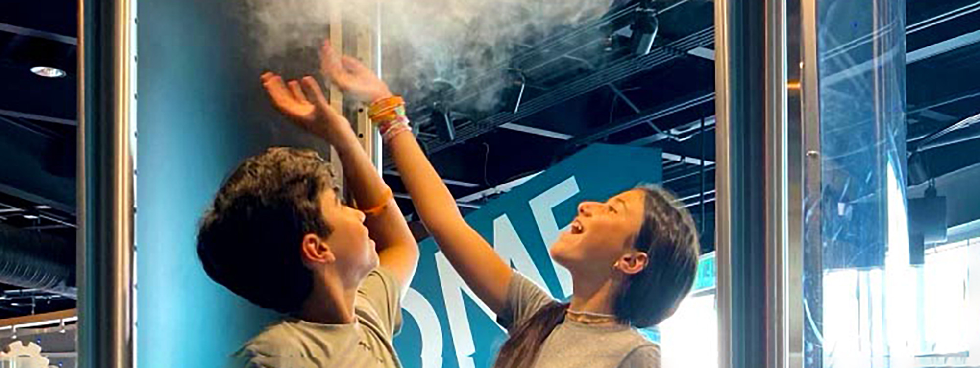 Two older kids smiling and reaching up to the tornado/air circulating in the vortex exhibit.