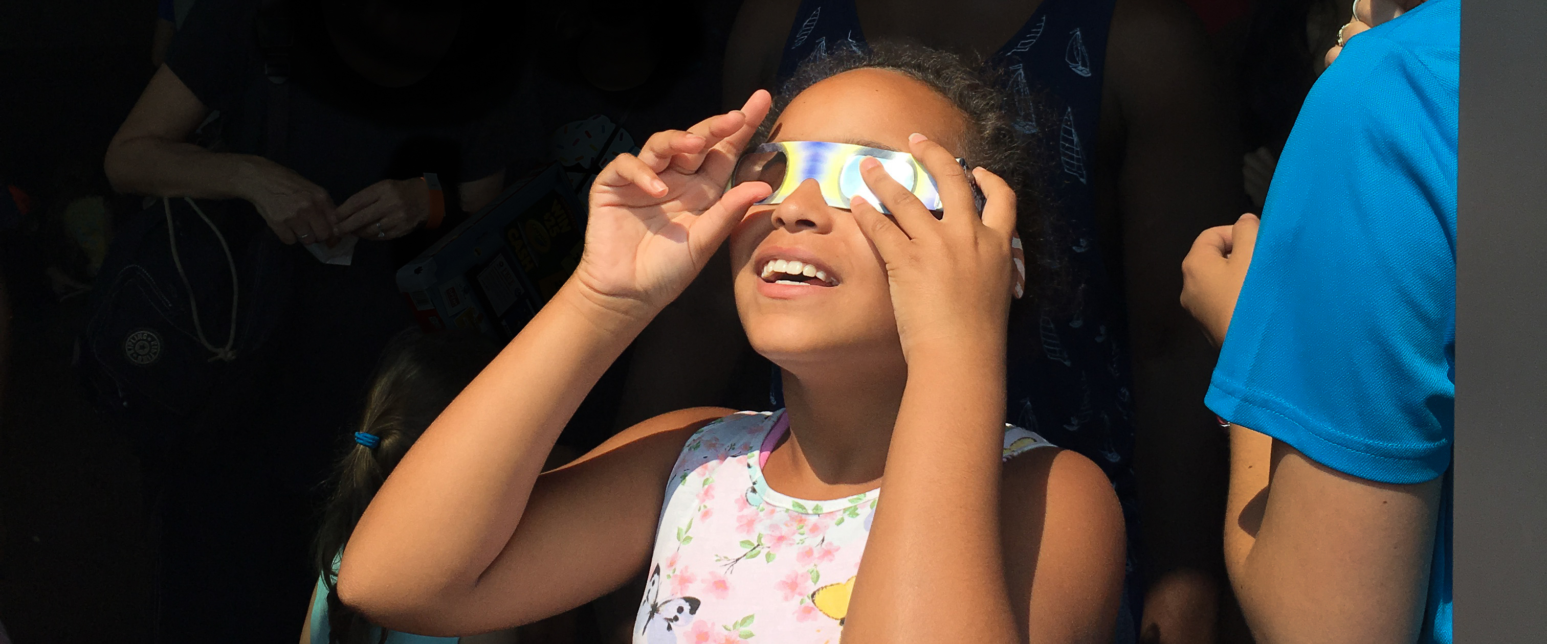Photo of a young girl using eclipse glasses to look at the sky.
