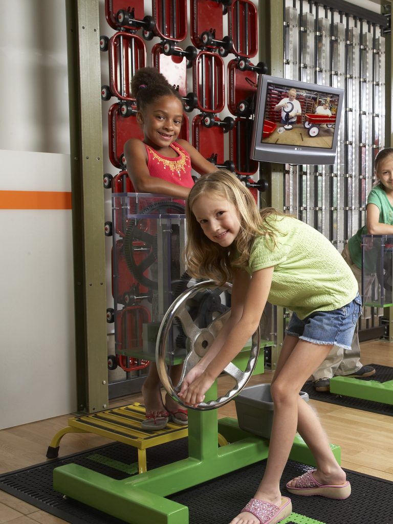 Two children use a hand crank to deform a penny.
