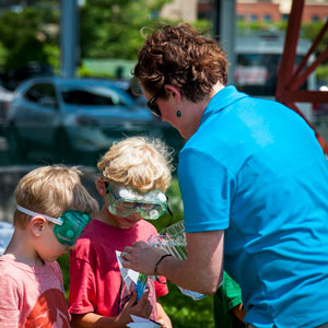 An ECHO staff member shows an experiment to two campers wearing safety goggles. 
