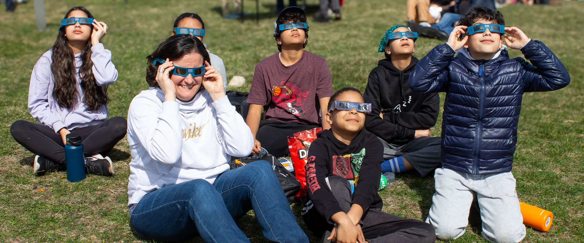 A group of ECHO guests of all ages look up at the eclipse through their glasses