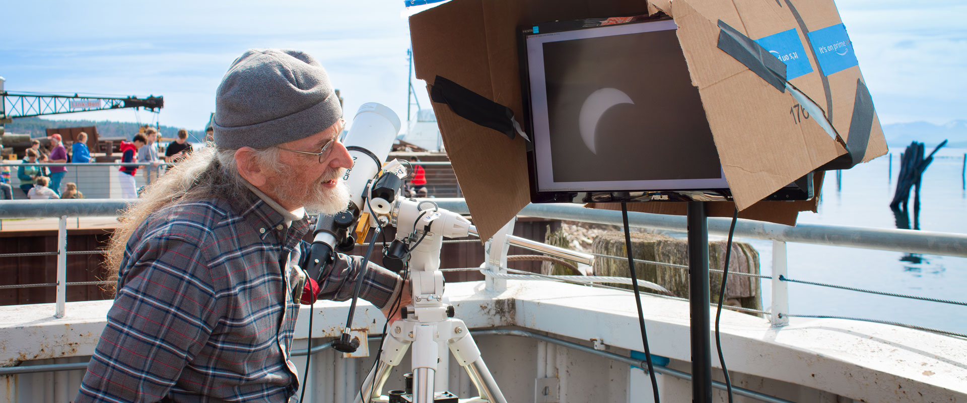 Jack from Vermont Astronomical Society stands next to a telescope while examining a monitor shielded by a cardboard box.