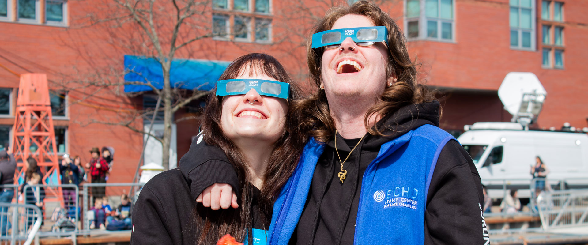 Two ECHO staff members watch the eclipse with smiles. One is holding a partially eaten tomato.