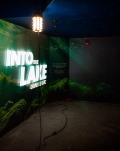The entryway of the Into the Lake exhibit, currently under construction. Large illuminated letters read "Into the Lake" and a large photographic mural of an under-the-lake scene covers the walls.