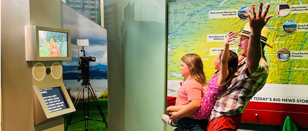 Family leans back with arms up in front of WCAX Lake News exhibit